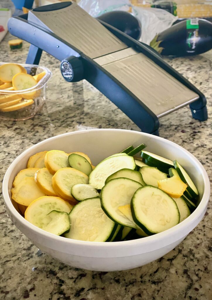 A bowl of sliced zucchini beside a mandolin