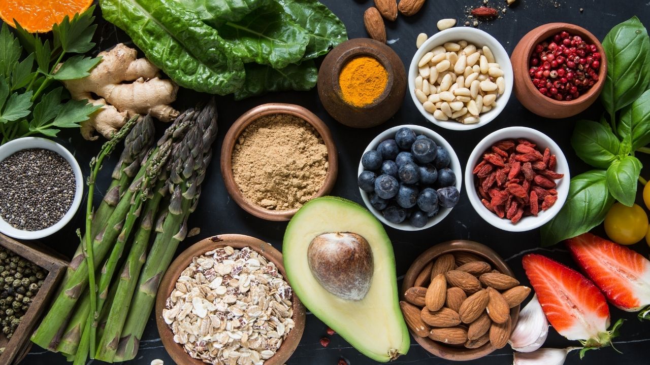 Overhead view of a variety of healthy foods including avocado, oatmeal, asparagus, blueberries, goji berries, almonds, and chia seeds.