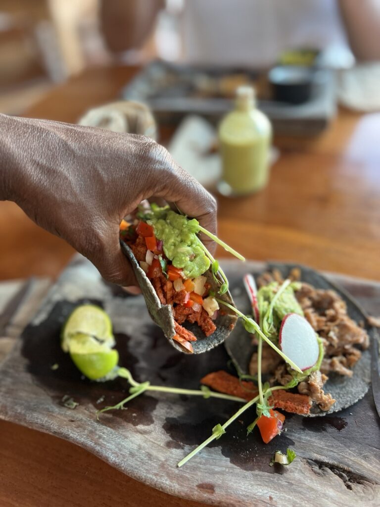 hand holding a taco with two tacos on a plate