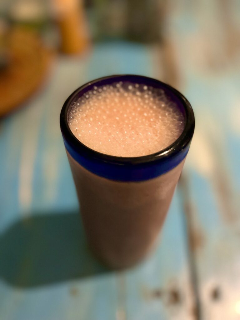 a glass on a table with a pink drink in it