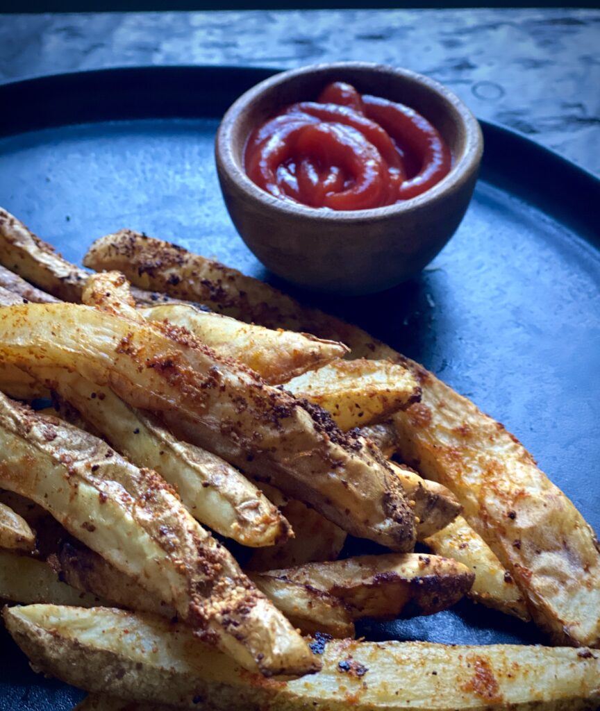 Close up picture of French fries and a small bowl of ketchup on a plate.