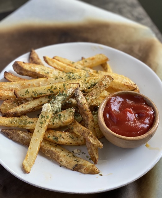 A plate of French fries with a small bowl of ketchup on the plate.