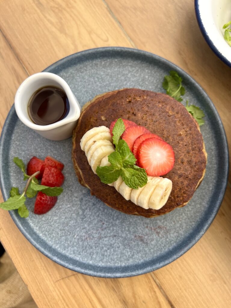 overhead view of plate of pancakes with sliced bananas and strawberries on top with a side of syrup.