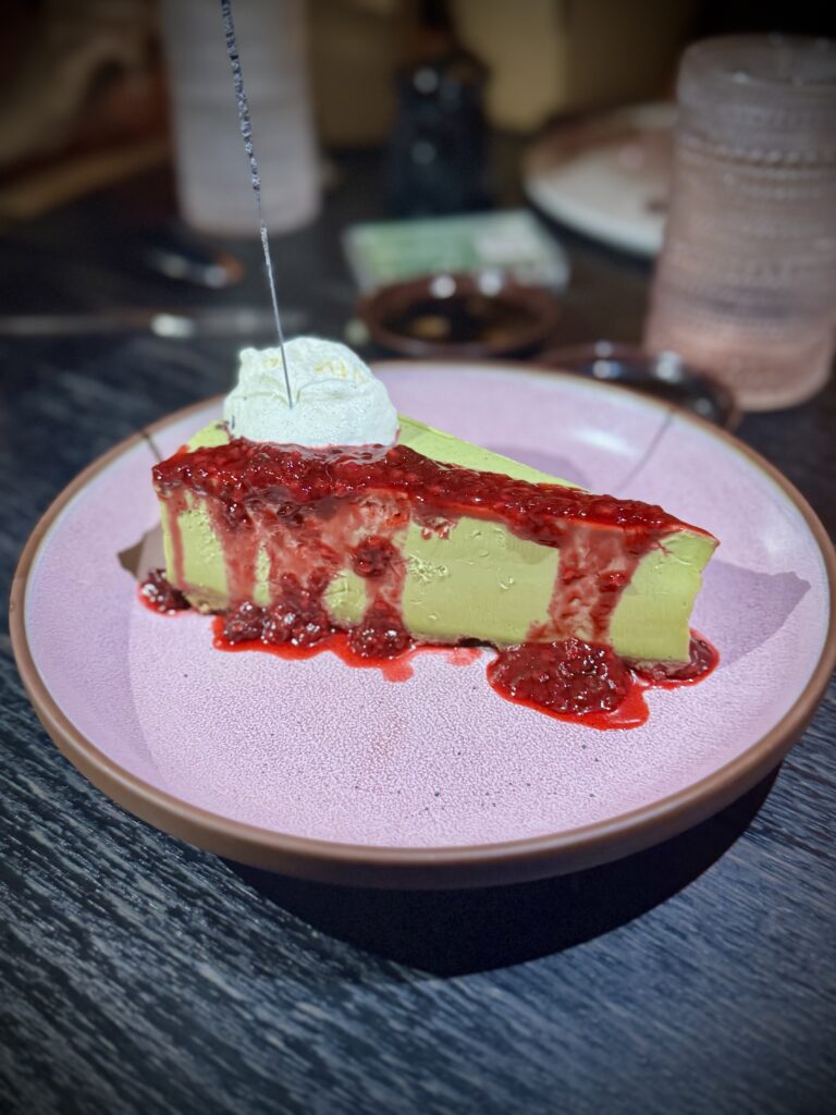 Matcha cheesecake topped with strawberry sauce and a dollop of whipped cream.