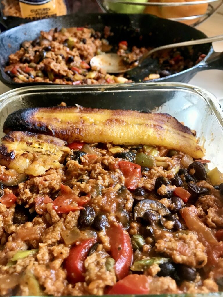 Casserole dish with pastelon filling with plantain slices being layered on top.