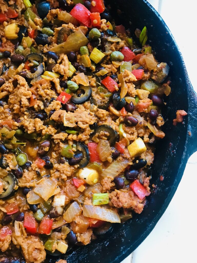 Cast iron pan filled with pastelon filling comprised of ground vegan beef, black olives, onions, bell peppers 
