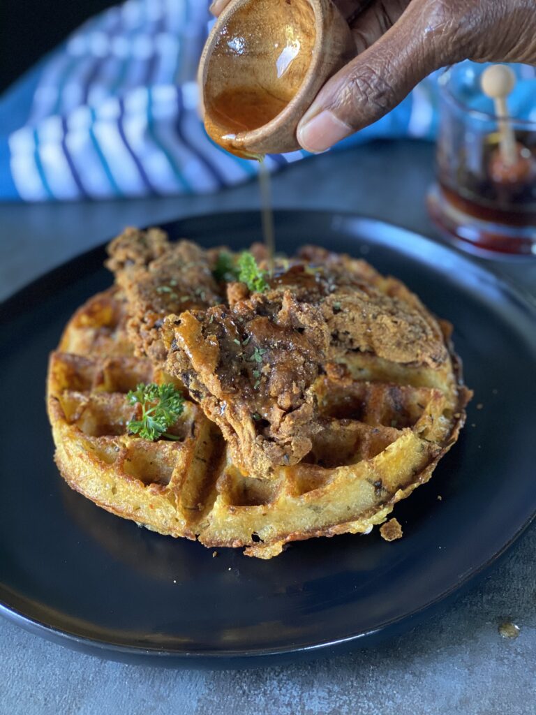 Picture of hot honey being poured onto a mashed potato waffle topped with air fried oyster mushrooms,
