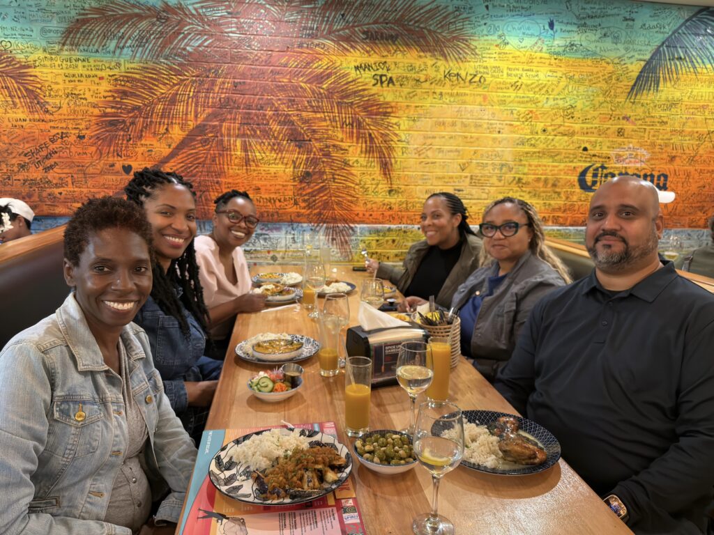 Photo of a group of people (5 women and one man) sitting at a table with meals in front of them, about to eat.