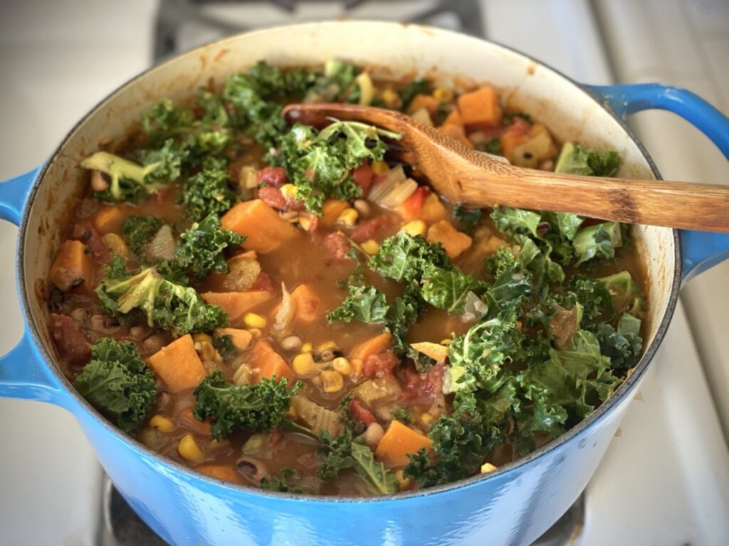 Soul food soup in a blue Dutch oven with a wooden spoon inside.