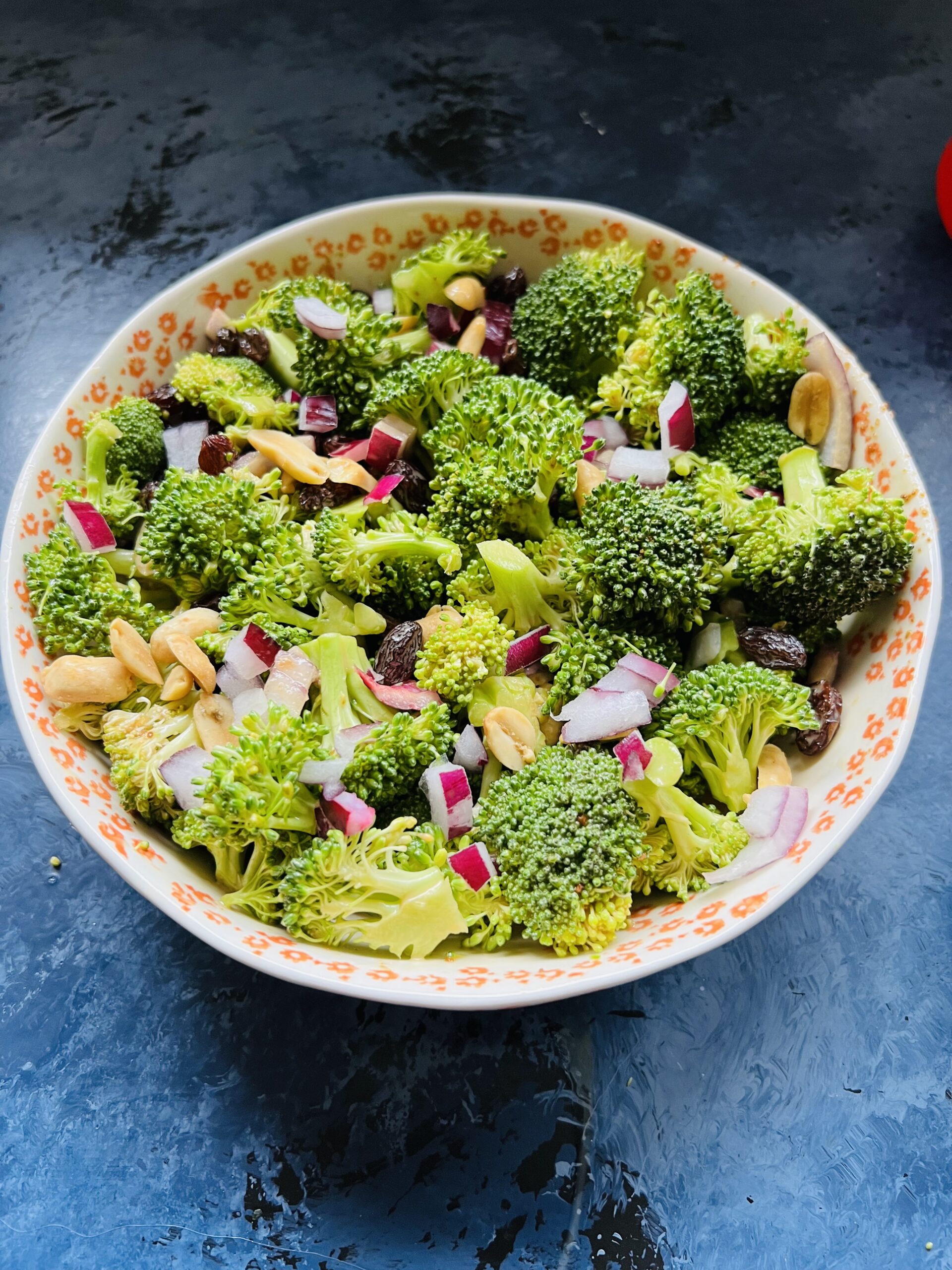 Bowl of broccoli salad wit peanuts, raisins and red onions.