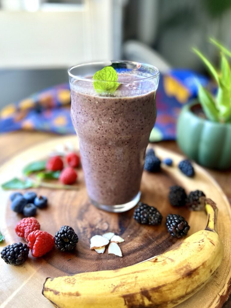 Glass of chia berry smoothie on a wooden slab surrounded by fresh blueberries, raspberries, and a banana.