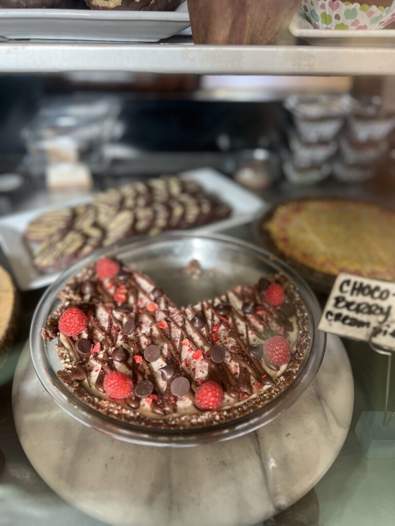 Raw coco-berry cream pie with a slice missing sitting in a shop display case.