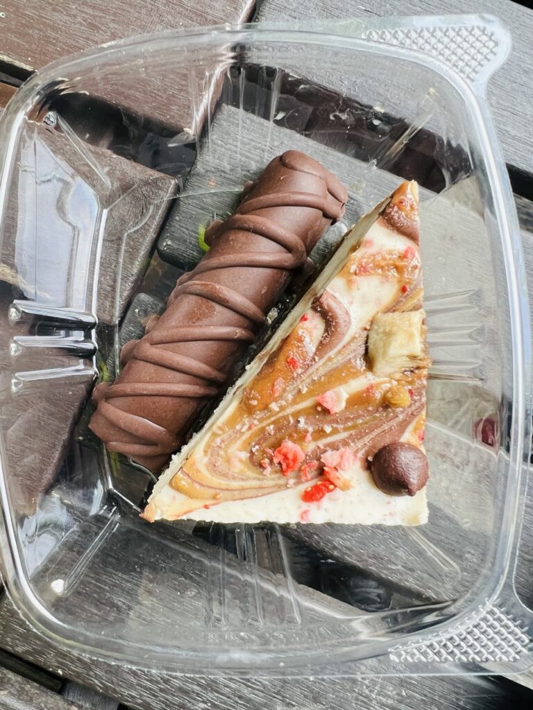 Plastic take-out container with a raw vegan Twix bar and a slice of chocolate berry pie