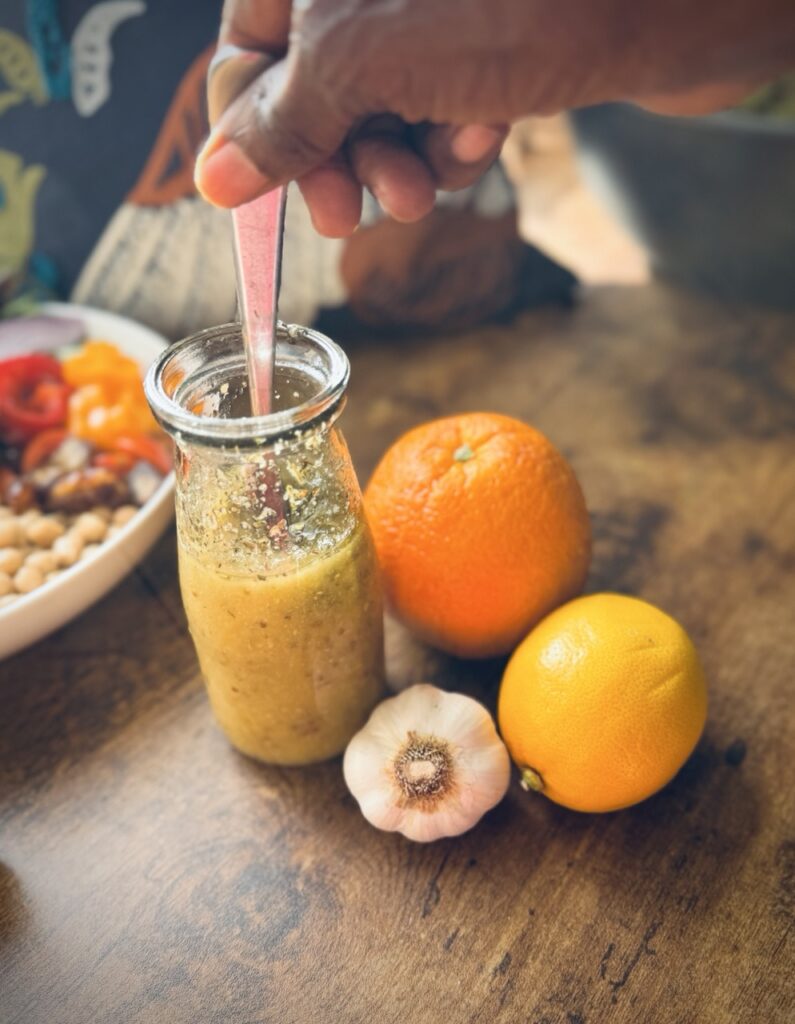 A bottle with salad dressing with a whole orange, whole lemon and a bulb of garlic beside it.
