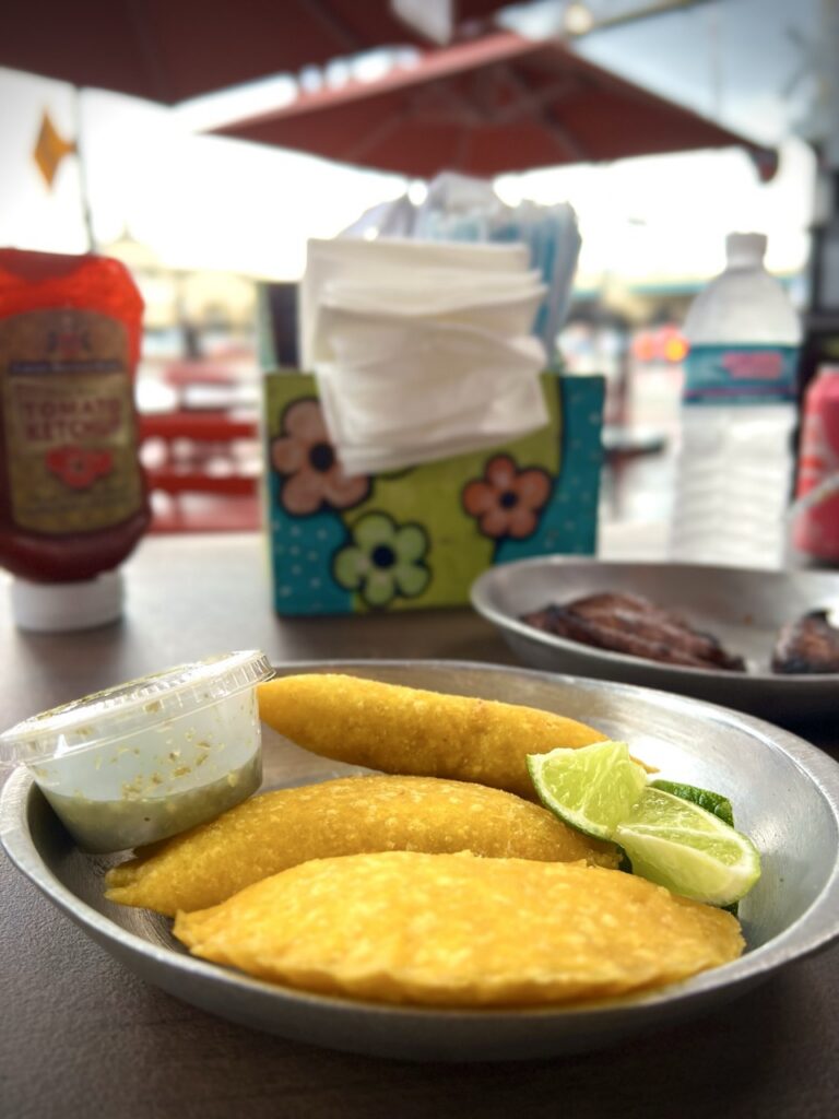 A metal bowl with 3 lentil empanadas  served with a small container of sauce and 2 wedges of lime.