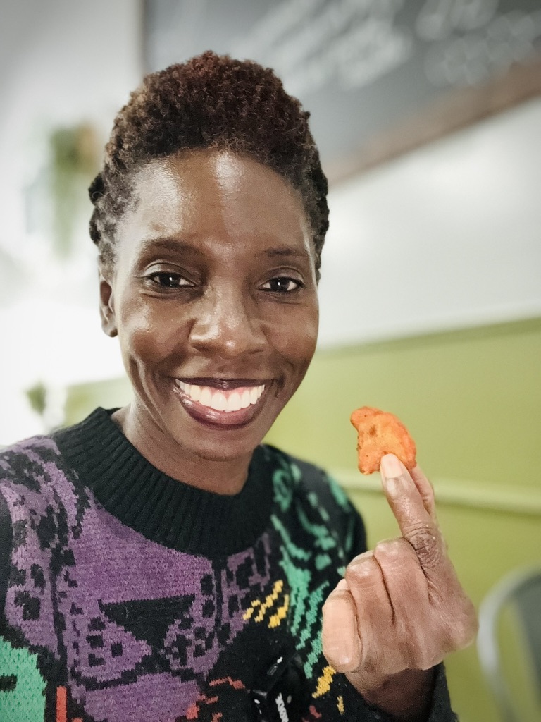 Woman in a colorful sweater holding a piece of fried cauliflower.
