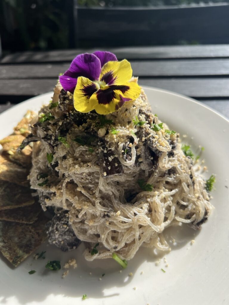 A plate of mushroom stroganoff made with kelp noodles and topped with purple and yellow edible flowers.