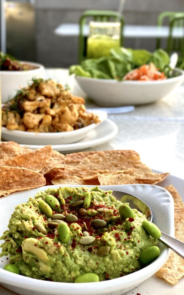 Spread with edamame guacamole in the foreground, charred cauliflower and a salad in the background.