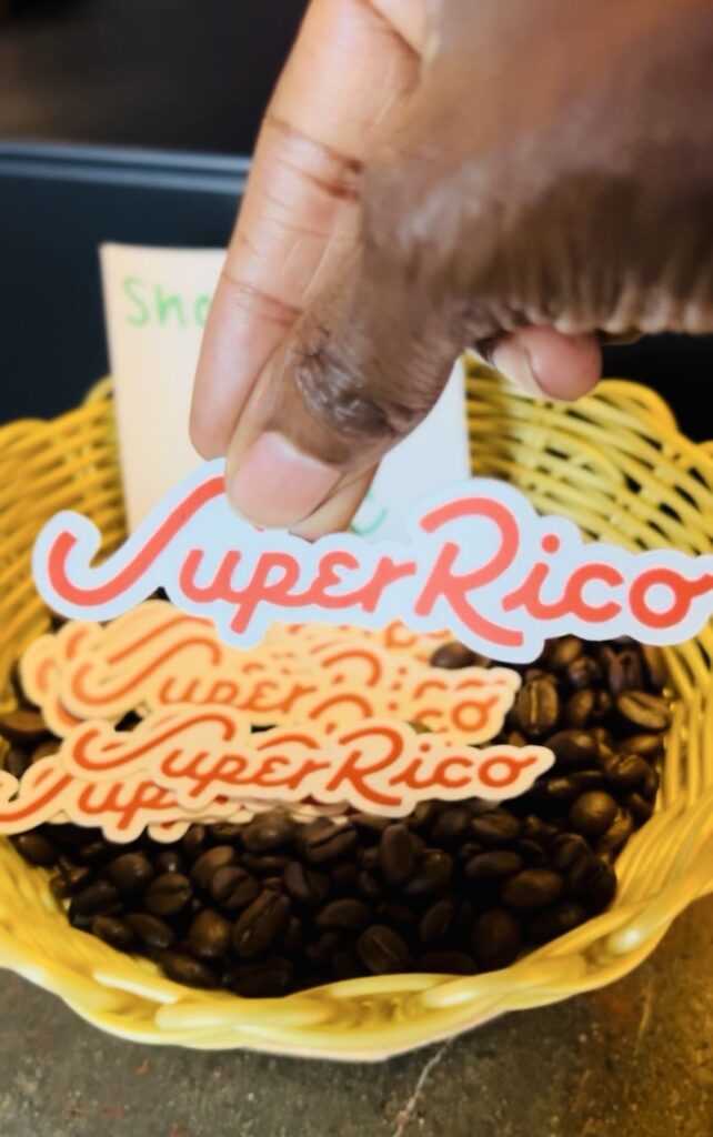 Picture of hand holding paper cut-outs that say Super Rico over a basket filled with coffee grounds.