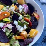 Bowl of roasted beet salad with golden and red beets, arugula, red onion, orange segments and vegan feta.