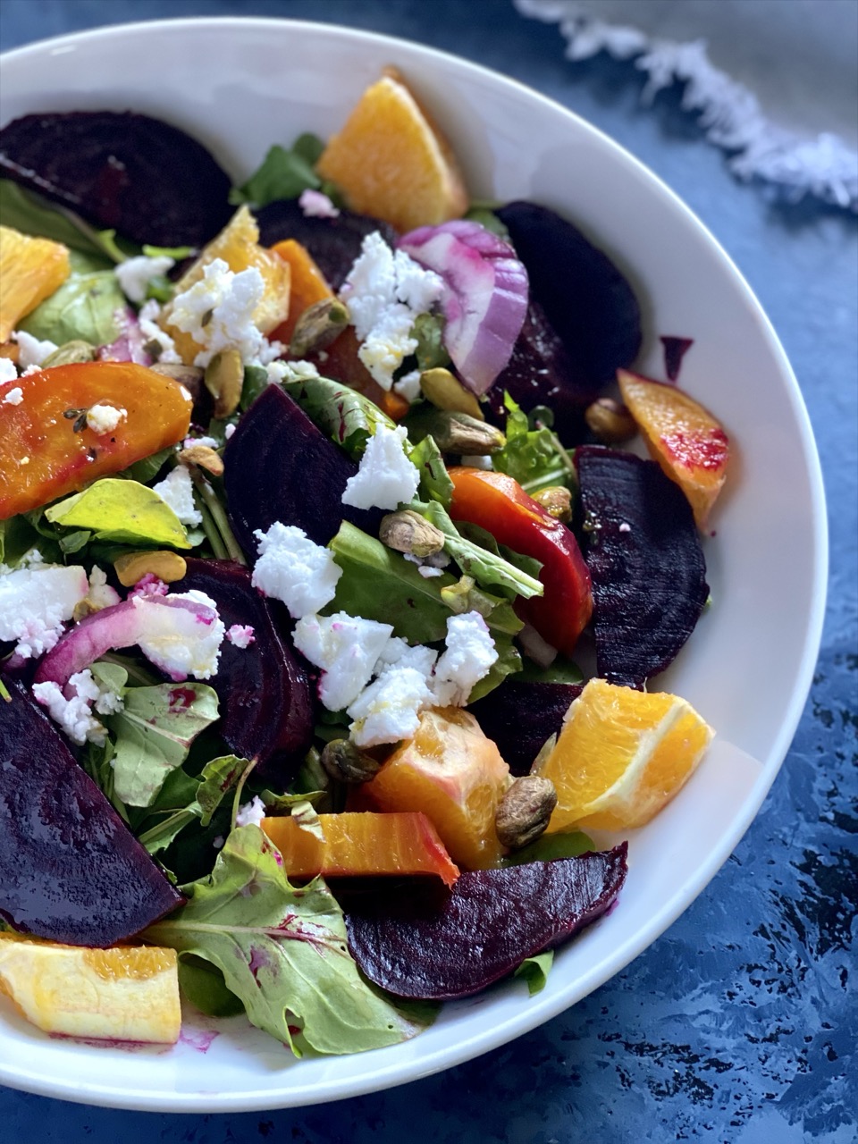 Bowl of roasted beet salad with golden and red beets, arugula, red onion, orange segments and vegan feta.