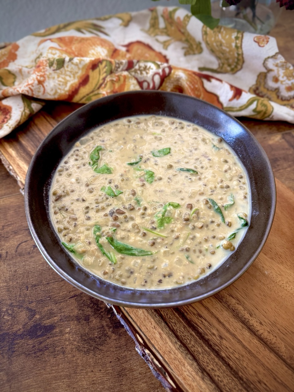 Bowl of mung bean soup sitting on a wooden plank on top of a wooden table with a cloth napkin beside it.