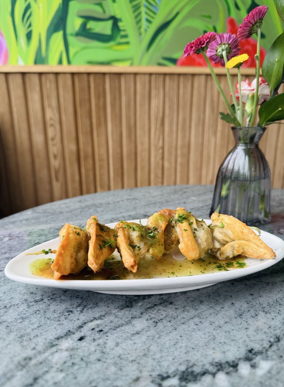 Plate of vegan curry chicken wontons on a table with a vase of flowers in the background.
