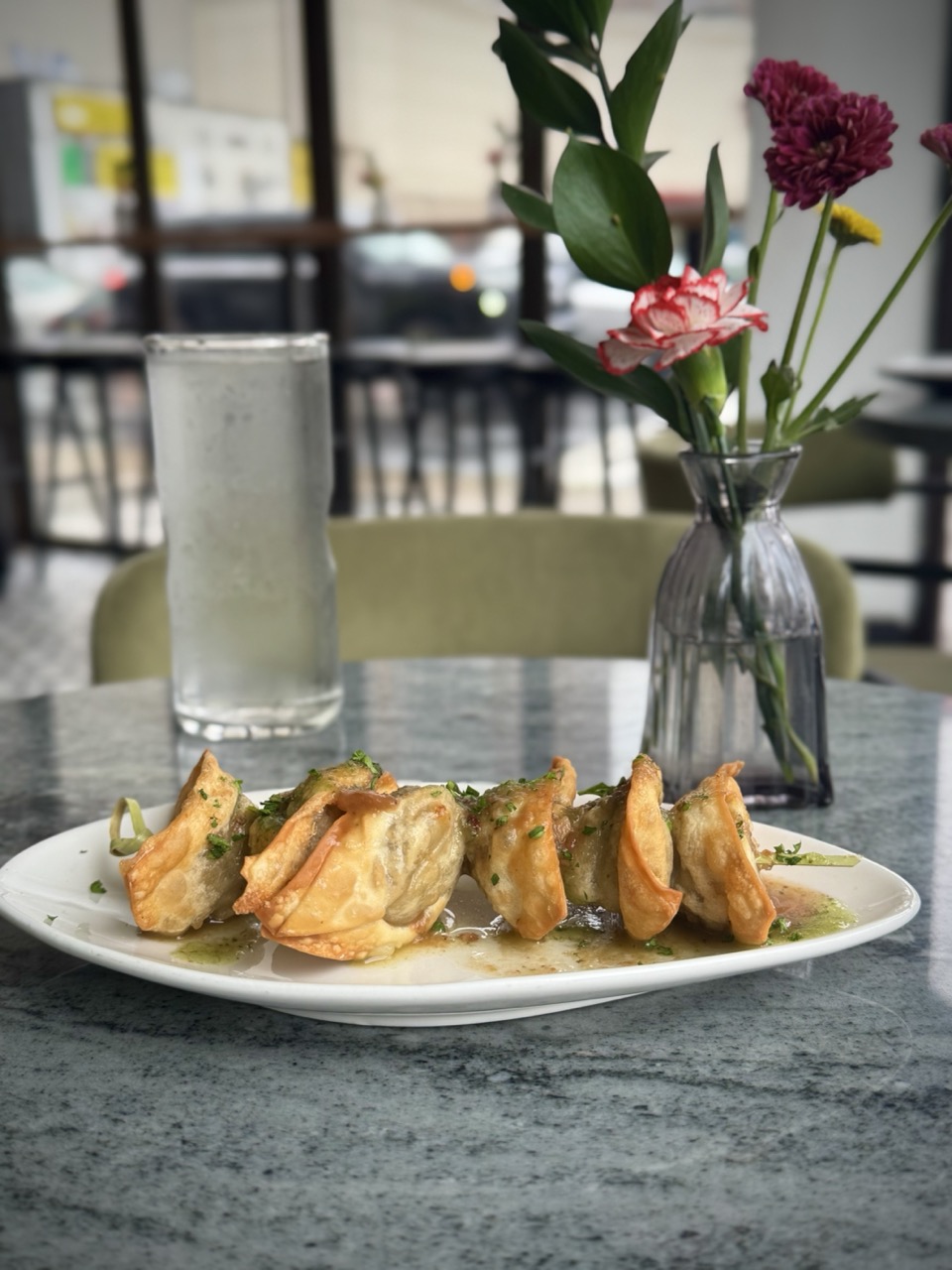 Plate of vegan curry chicken wontons on a table with a vase of flowers in the background.