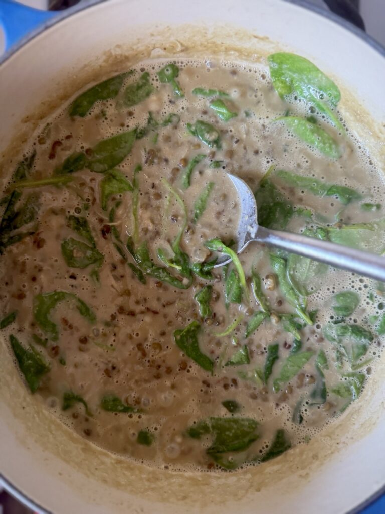 Overhead shot of a pot of mung bean soup with wilted spinach being stirred by a spoon.