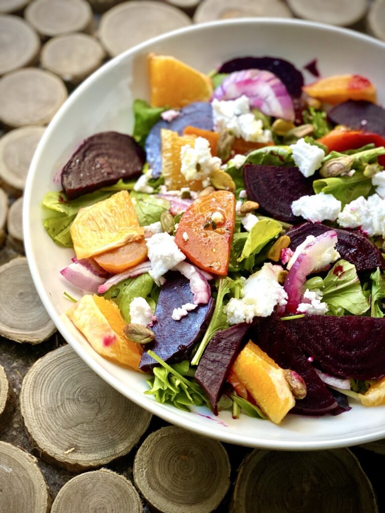 Bowl of roasted beet salad with golden and red beets, arugula, red onion, and vegan feta.