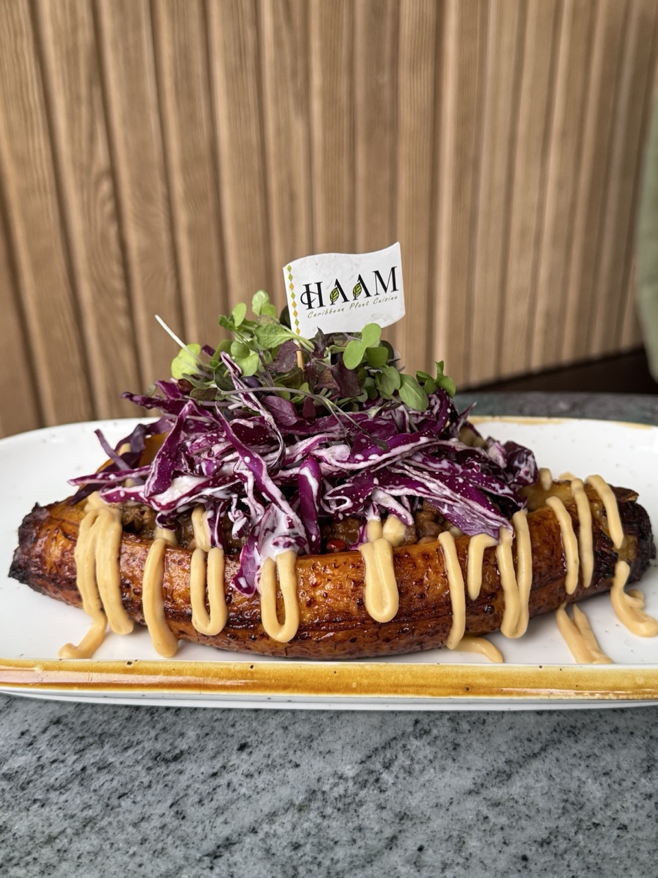 Plantain boat filled with vegan ground beef and topped with purple cabbage slaw, micro greens, with an orange creamy sauce drizzled on top. 