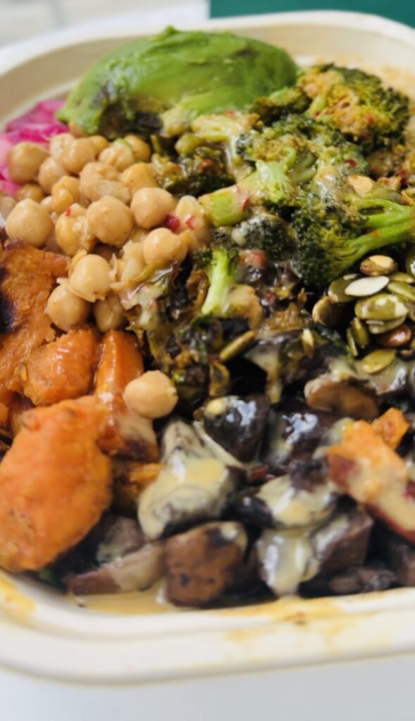 Bowl of vegetables from Sweet Green restaurant including chickpeas,pumpkin seeds, roasted Brussels sprouts, roasted broccoli,Roasted sweet potatoes, roasted Roasted portobello mushrooms, Chickpeas, half of an avocado and pickled red onions on a bed of spinach, quinoa and wild rice.