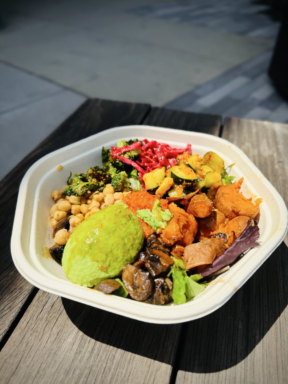 Bowl of vegetables from Sweet Green restaurant including avocado, butternut squash, chickpeas, Brussels sprouts, kimchi, cabbage, roasted broccoli and more.