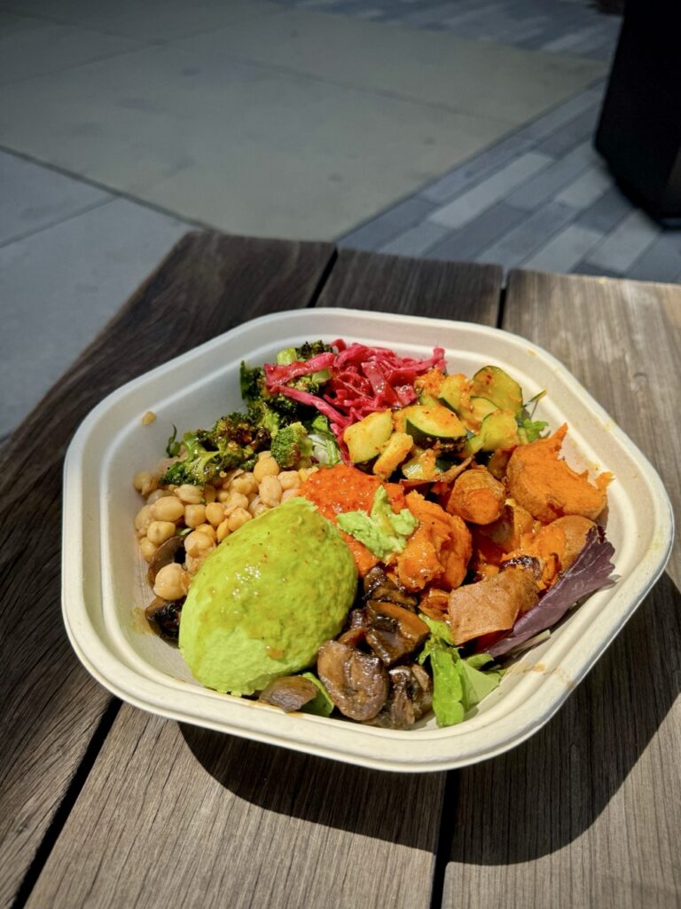 Bowl of vegetables from Sweet Green restaurant including avocado, butternut squash, chickpeas, Brussels sprouts, kimchi, cabbage, roasted broccoli and more.