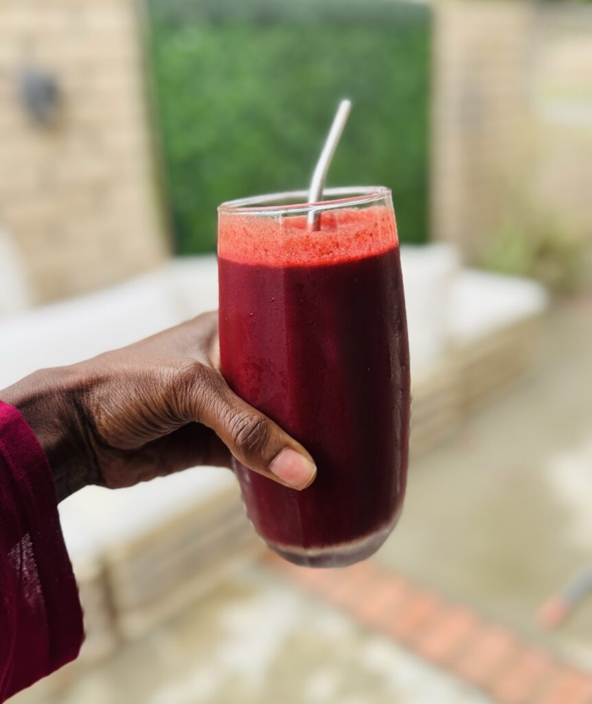 A hand holding a glass of ABC juice with a metal straw in it.