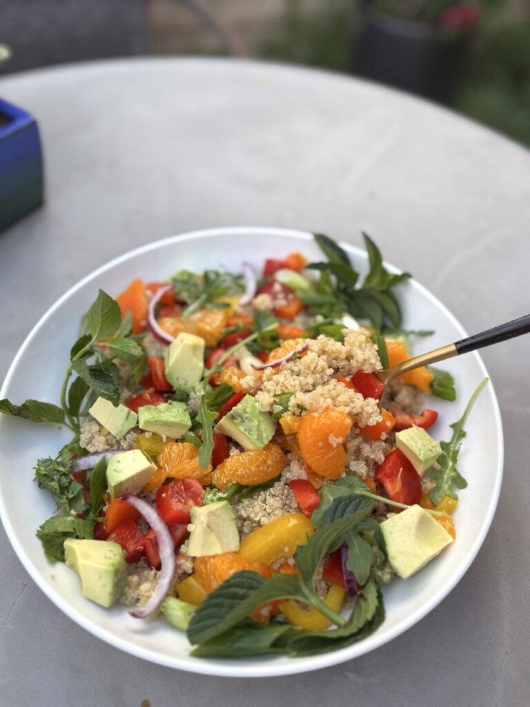 Bowl of Quinoa Citrus Salad with mandarin oranges, bell peppers, avocados, mint, arugula, scallion and arugula  
