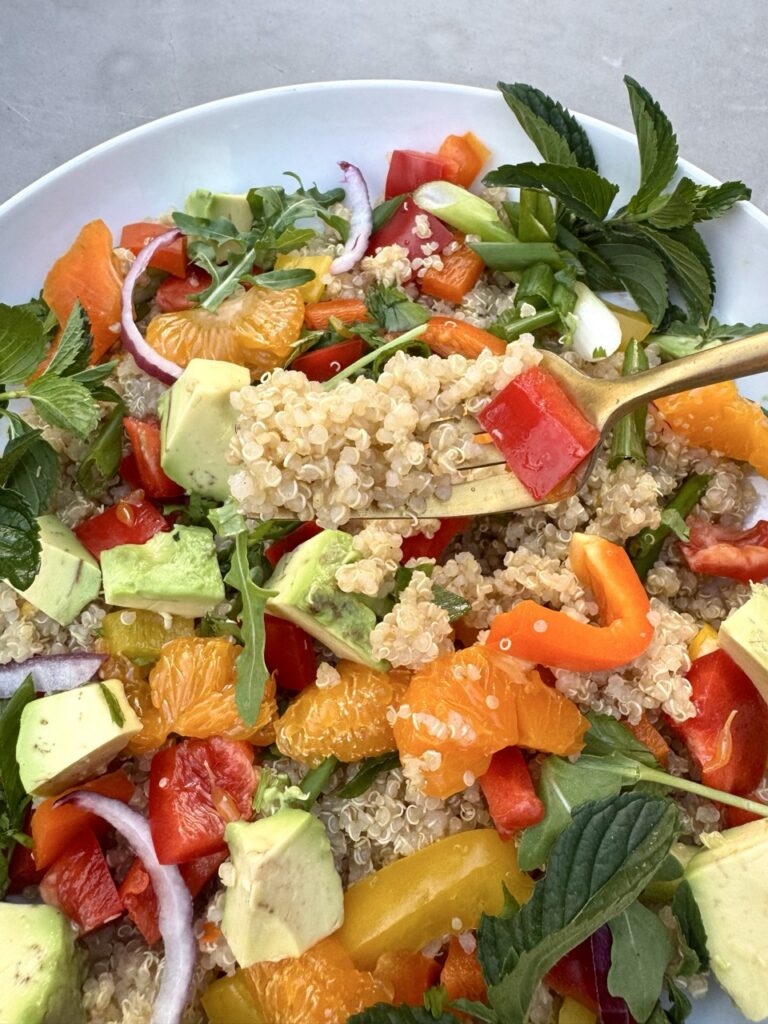Bowl of Quinoa Citrus Salad with mandarin oranges, bell peppers, avocados, mint, arugula, scallion and arugula  
