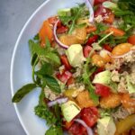 Bowl of Quinoa Citrus Salad with mandarin oranges, bell peppers, avocados, mint, arugula, scallion and cilantro.
