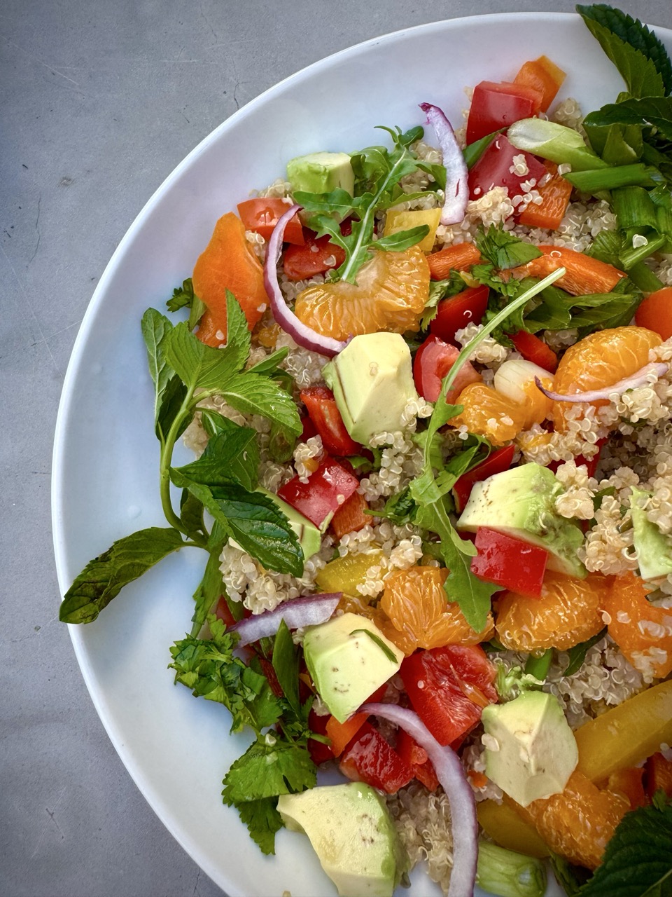 Bowl of Quinoa Citrus Salad with mandarin oranges, bell peppers, avocados, mint, arugula, scallion and cilantro.