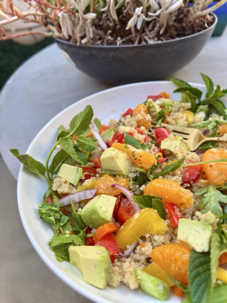 Bowl of Quinoa Citrus Salad with mandarin oranges, bell peppers, avocados, mint, arugula, scallion and cilantro.