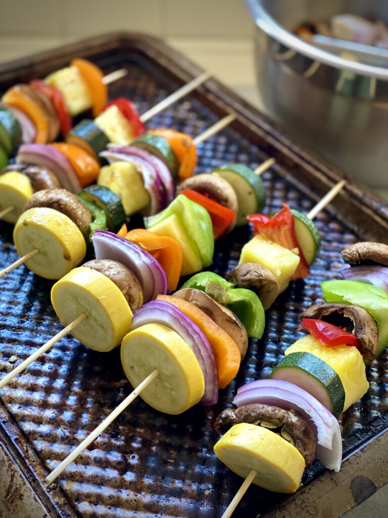 Jerk veggie kabobs with red onion, red bell peppers, green bell peppers, zucchini, orange bell peppers, and mushrooms on skewers.