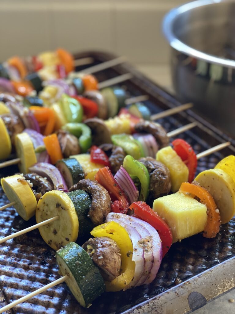 Jerk veggie kabobs with red onion, red bell peppers, green bell peppers, zucchini, orange bell peppers, and mushrooms on  skewers.