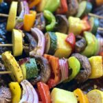 Jerk veggie kabobs with red onion, red bell peppers, green bell peppers, zucchini, orange bell peppers, and mushrooms on skewers.