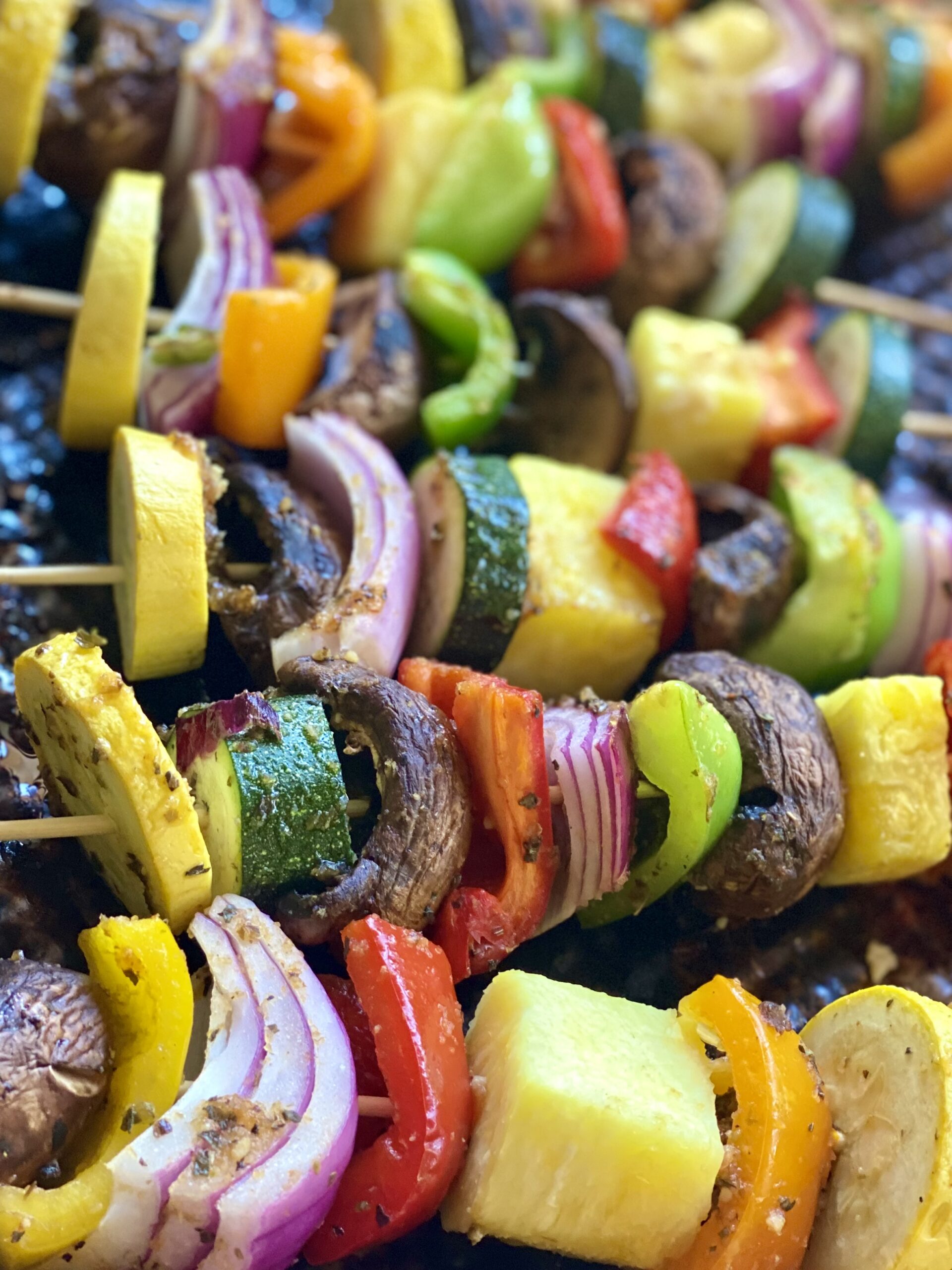 Jerk veggie kabobs with red onion, red bell peppers, green bell peppers, zucchini, orange bell peppers, and mushrooms on skewers.