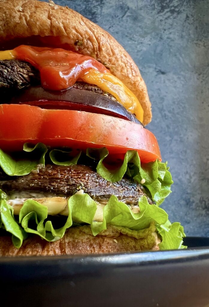 portobello mushroom sandwich on a wheat bun with melted cheese, ketchup, lettuce, tomatoes, and red onion.