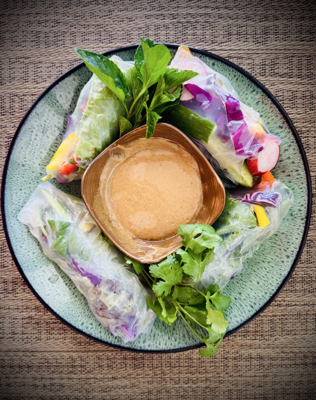 Summer rolls filled with bell peppers, red cabbage, lettuce, vermicelli, radishes, and cucumbers with bowl of peanut sauce.
