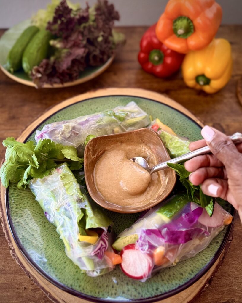 Summer rolls filled with bell peppers, red cabbage, lettuce, vermicelli, radishes, and cucumbers with bowl of peanut sauce.