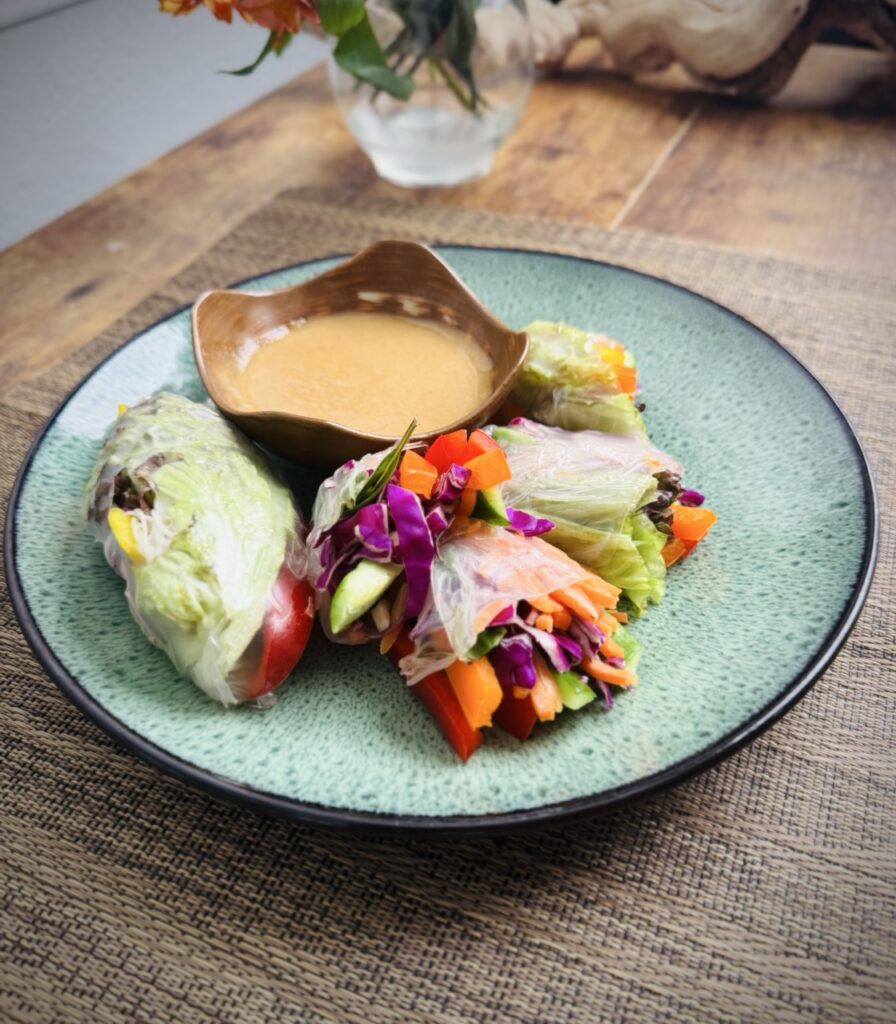 Summer rolls filled with bell peppers, red cabbage, lettuce, vermicelli, radishes, and cucumbers with bowl of peanut sauce.