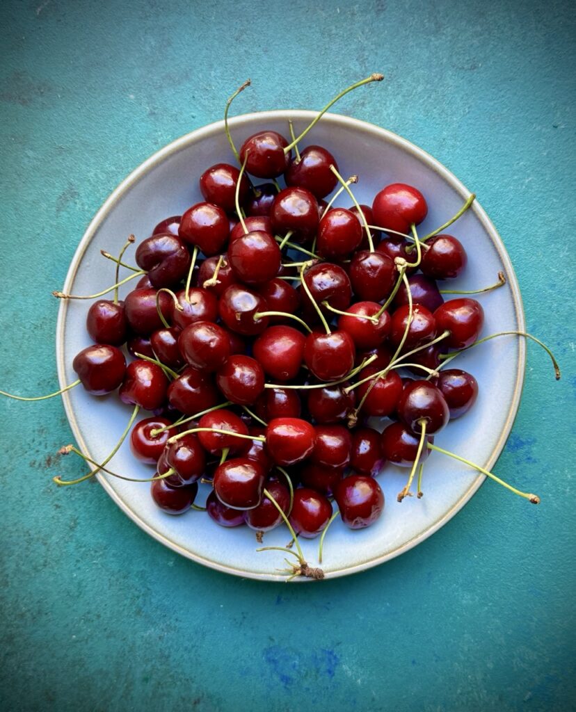 Bowl filled with cherries on  a green background