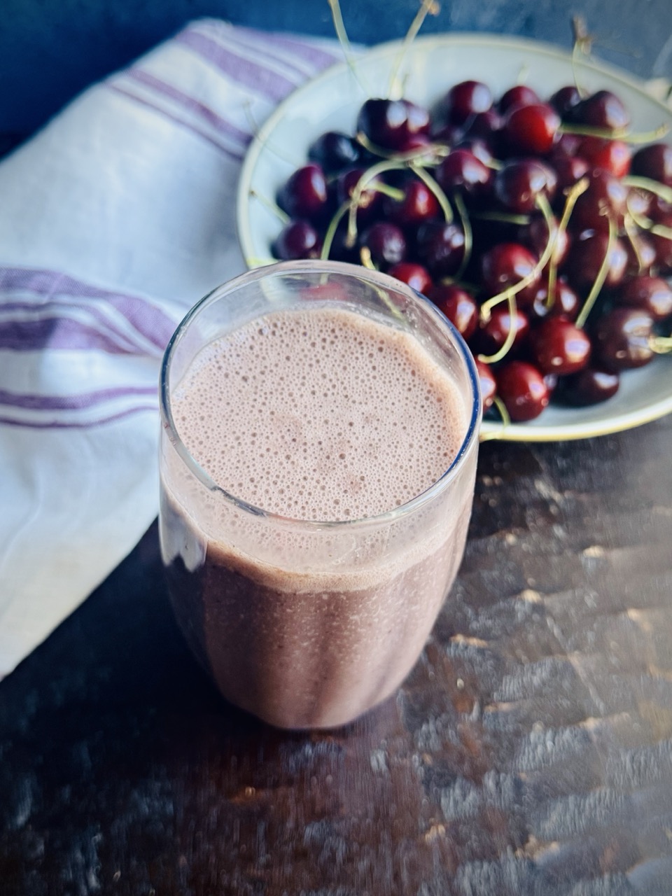 Glass filled with cherry smoothie with a bowl of cherries in the background.